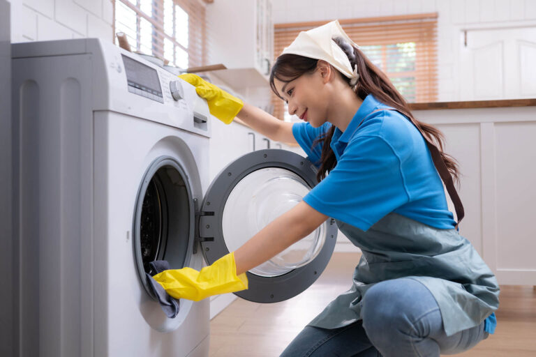 Professional cleaner in yellow gloves loading laundry into a washing machine for a fresh apartment or commercial space.