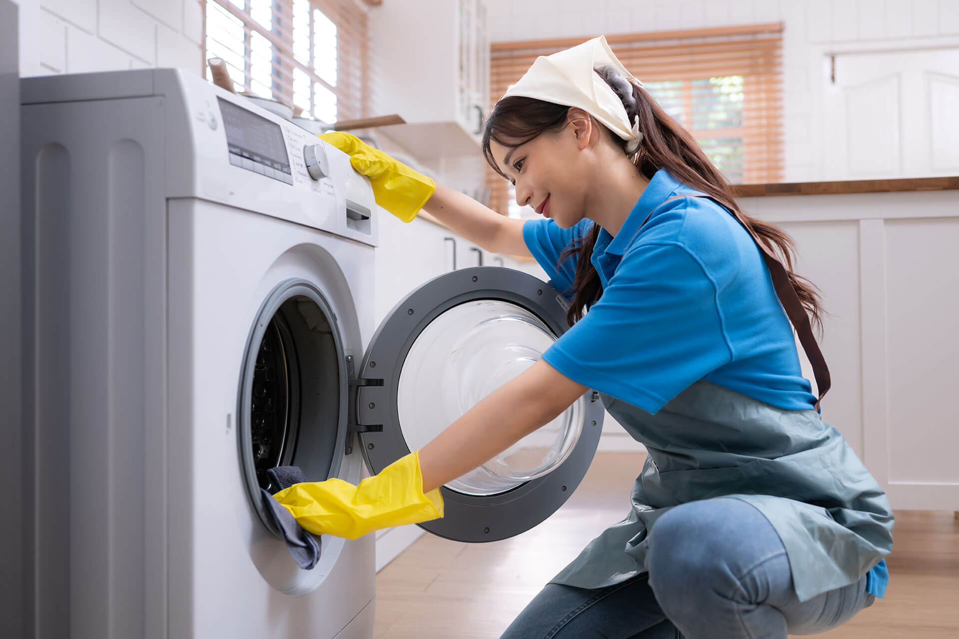 Professional cleaner in yellow gloves loading laundry into a washing machine for a fresh apartment or commercial space.