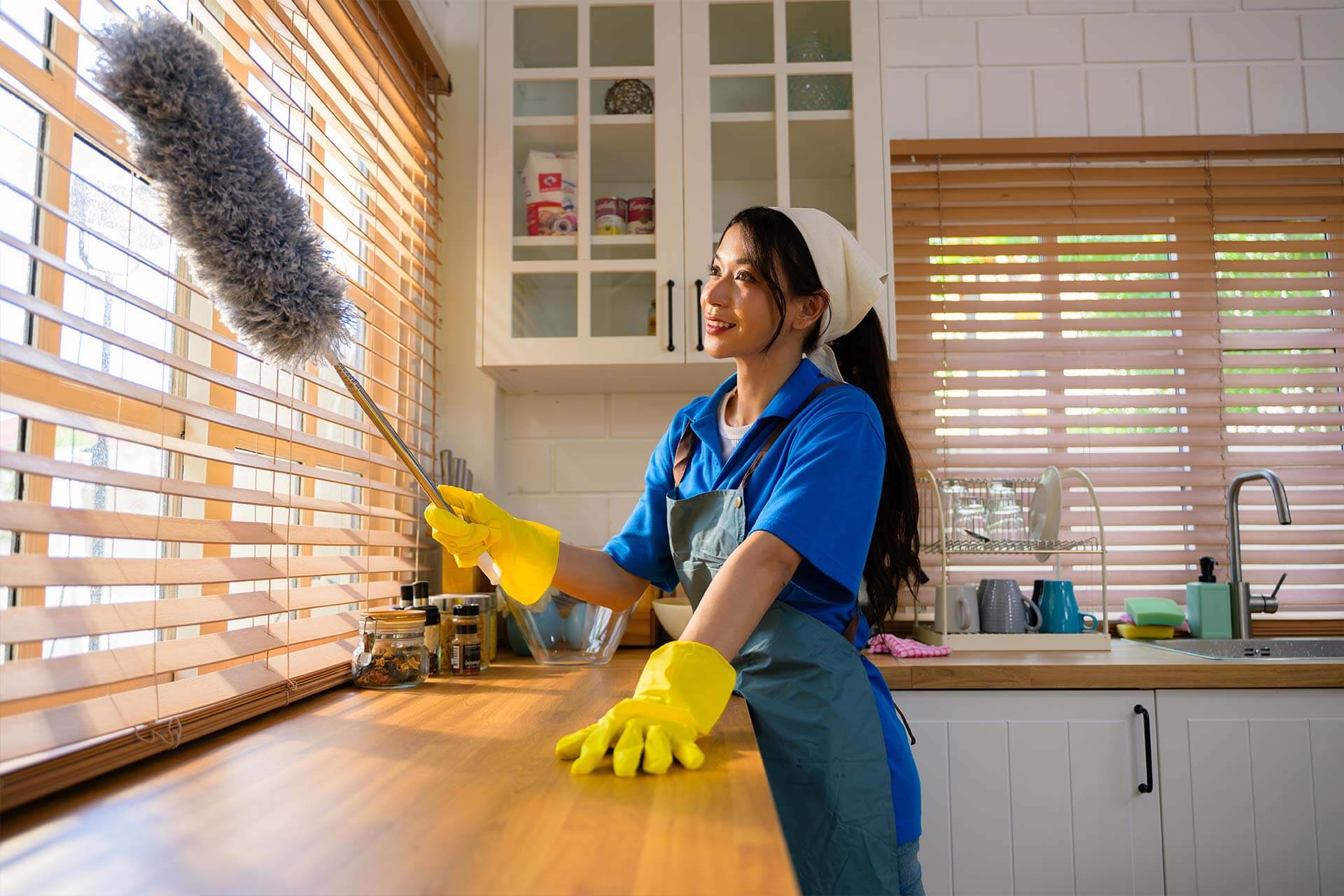 A Queen B Cleaning professional in yellow gloves dusting kitchen blinds, providing premium apartment and commercial cleaning for a fresh space.